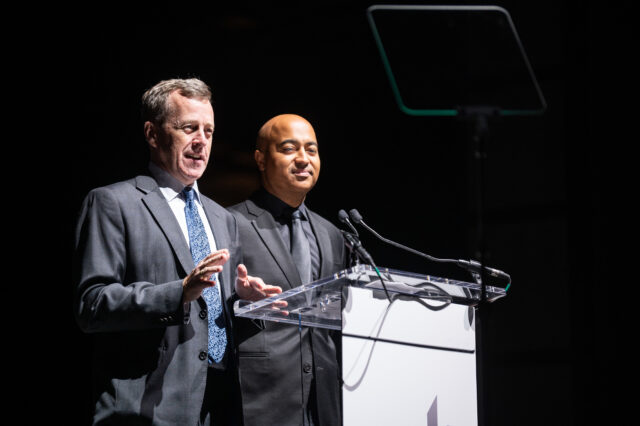 CDT board member Mark Seifert speaks from the podium at Tech Prom 2022, while board member Travis LeBlanc looks on.